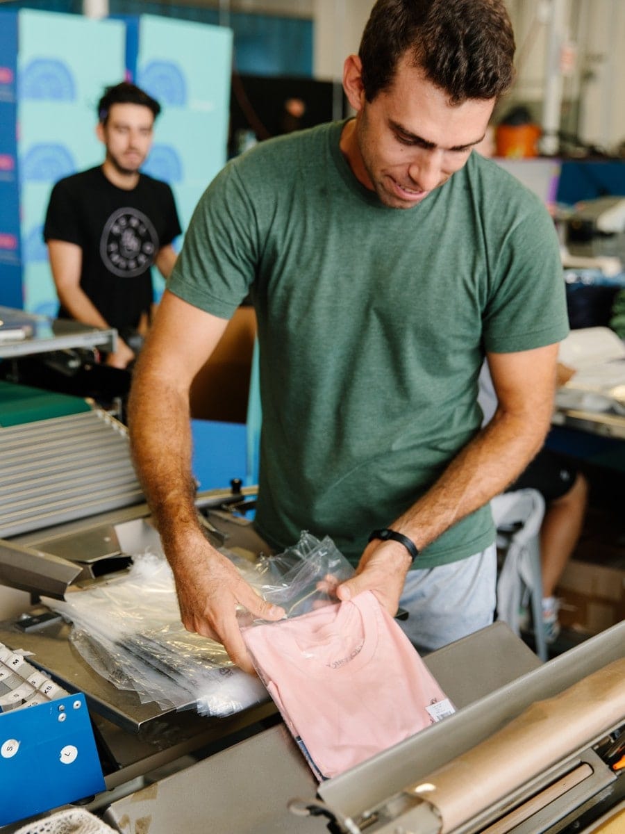 A man prepares a shirt for fulfillment, packing it in a polybag to keep it tidy.