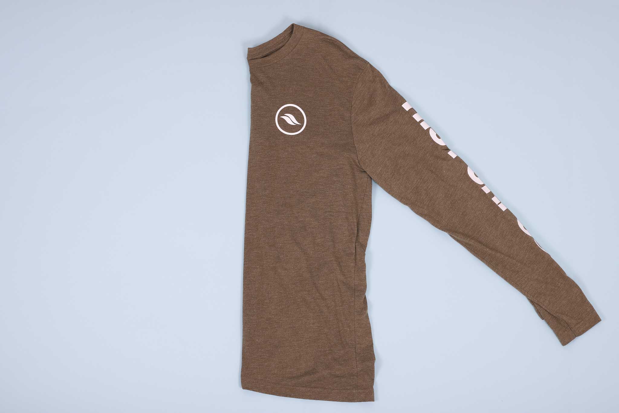 Olive long sleeve shirt with white text on the sleeves folded in half on a light blue background