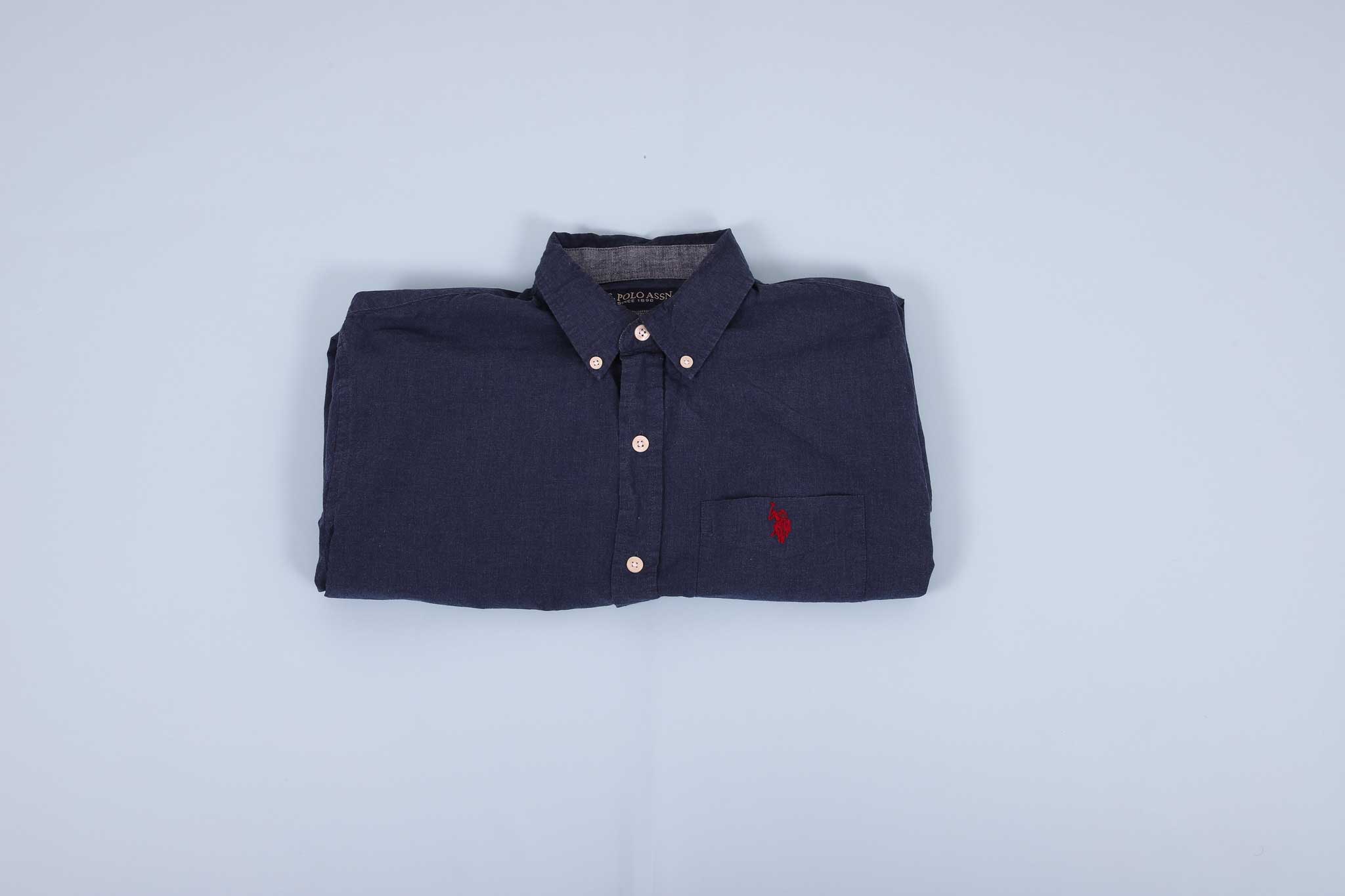 Navy buttoned up shirt folded into thirds agains a light blue background