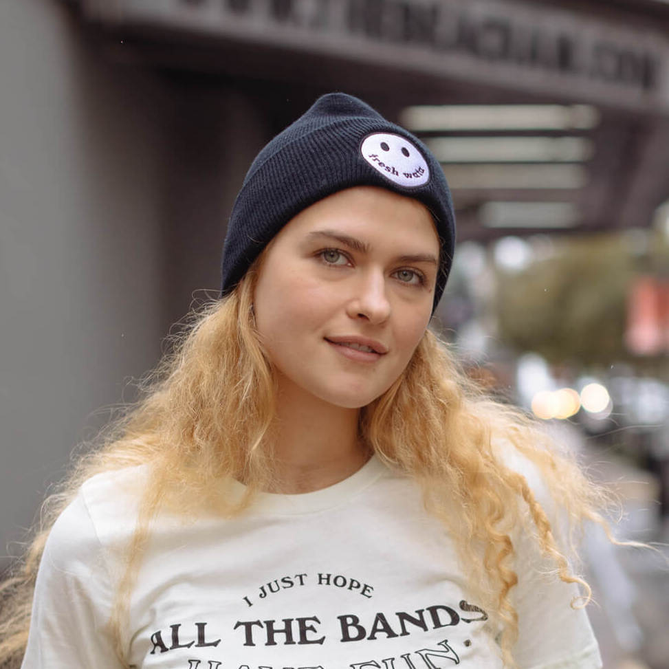 Woman wears a black beanie with an embroidered smiley face