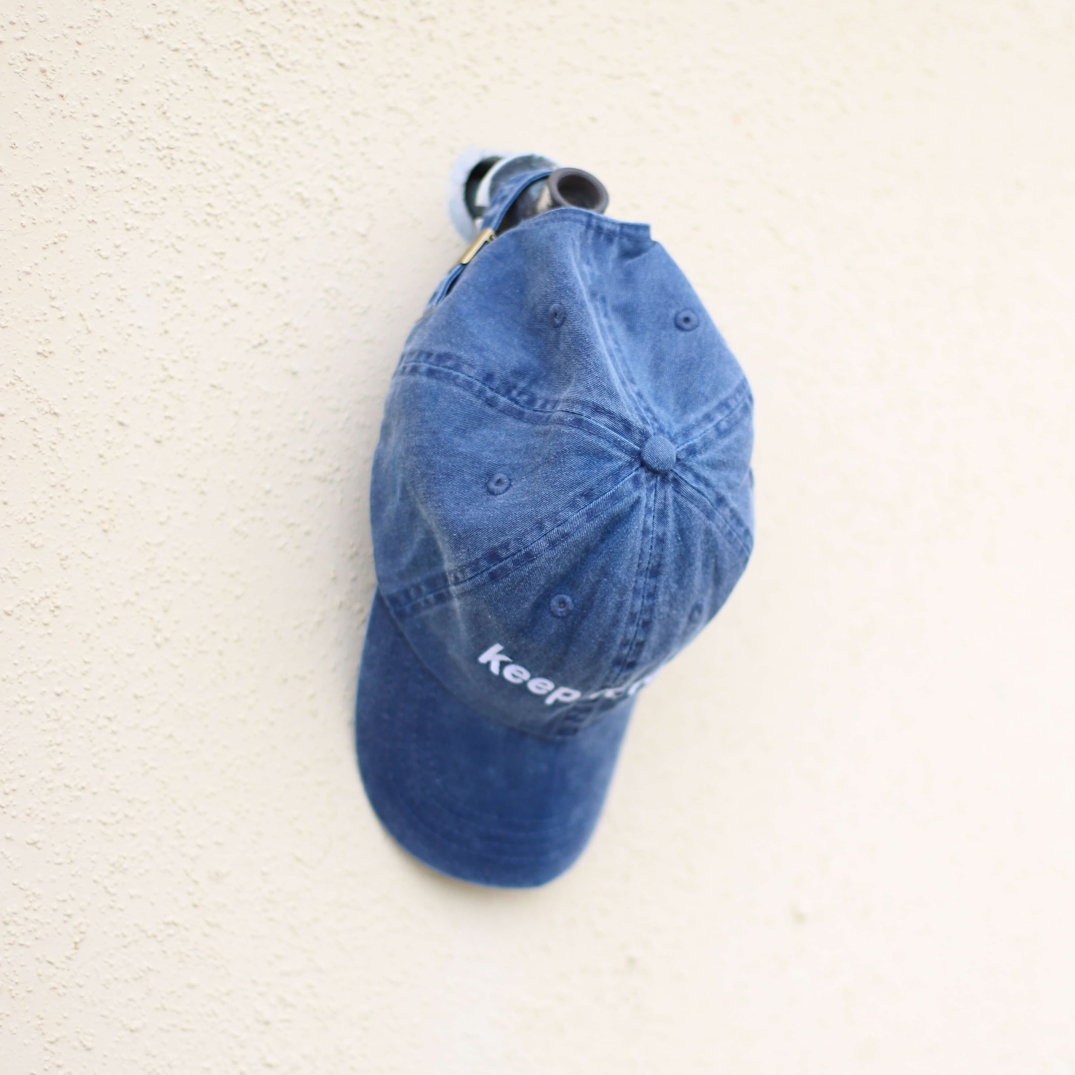 A blue baseball cap hangs on a hook on a wall